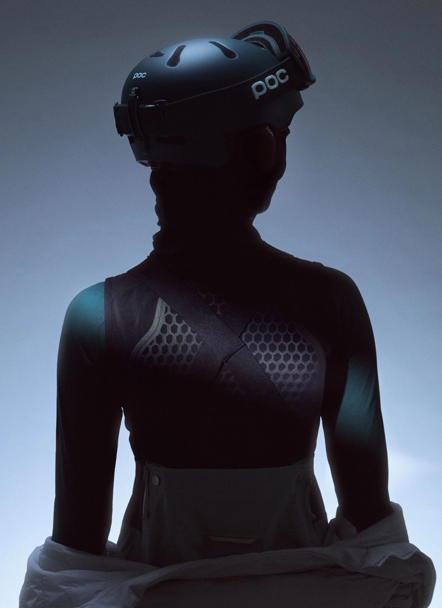 Woman in silhouette wearing black ski helmet and protective race suit against blue sky