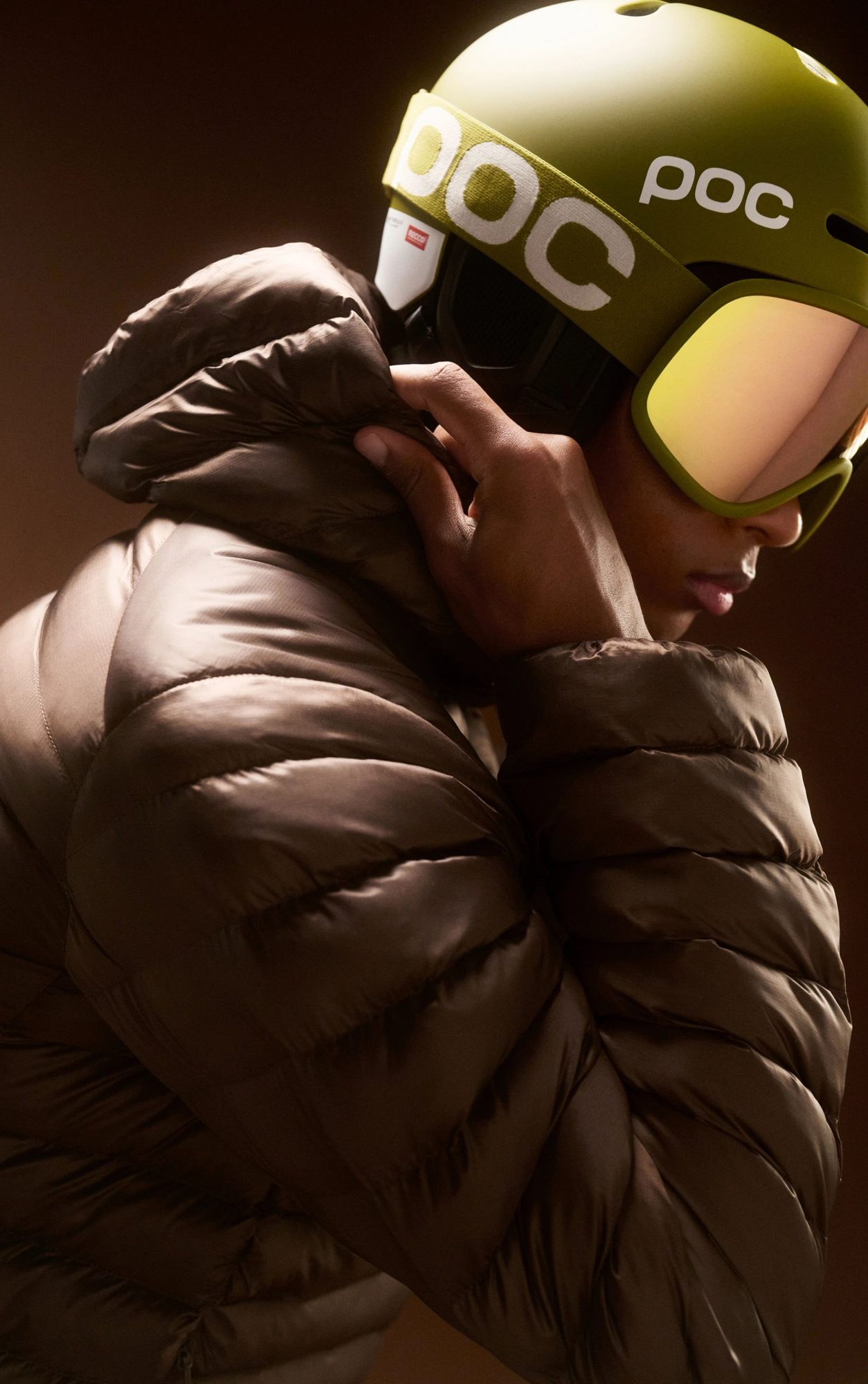 Person wearing a yellow-green ski helmet and dark jacket with goggles pushed up on helmet