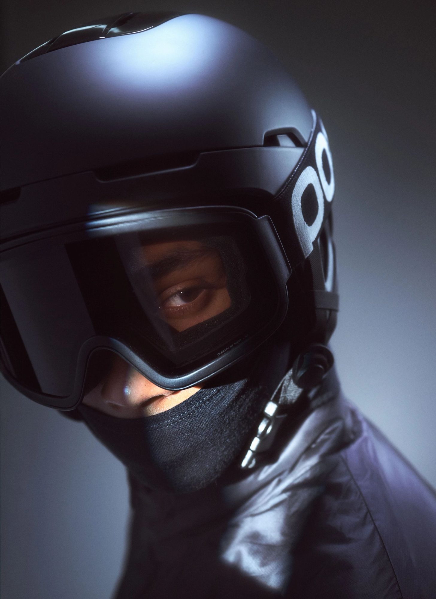 Close-up of person wearing black ski helmet with dark goggles and neck gaiter